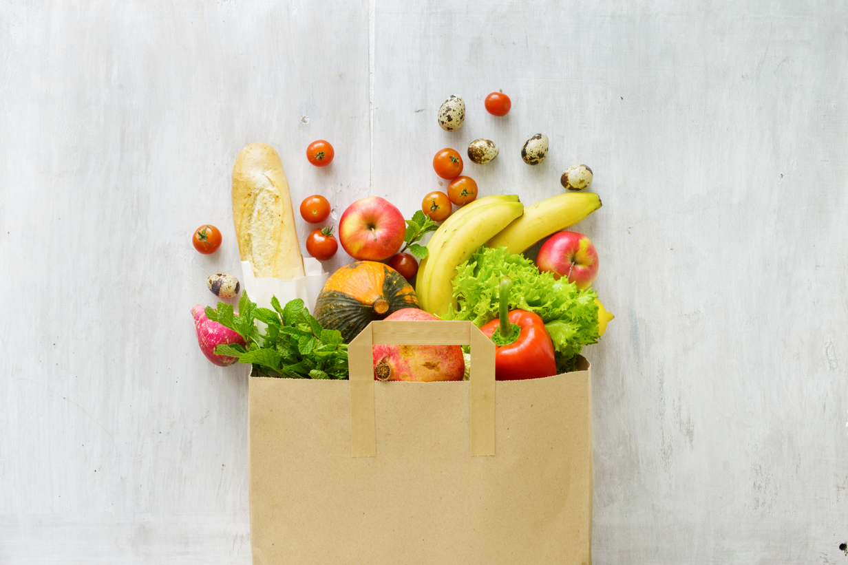 Top view paper bag of different fresh health food on white wooden background.